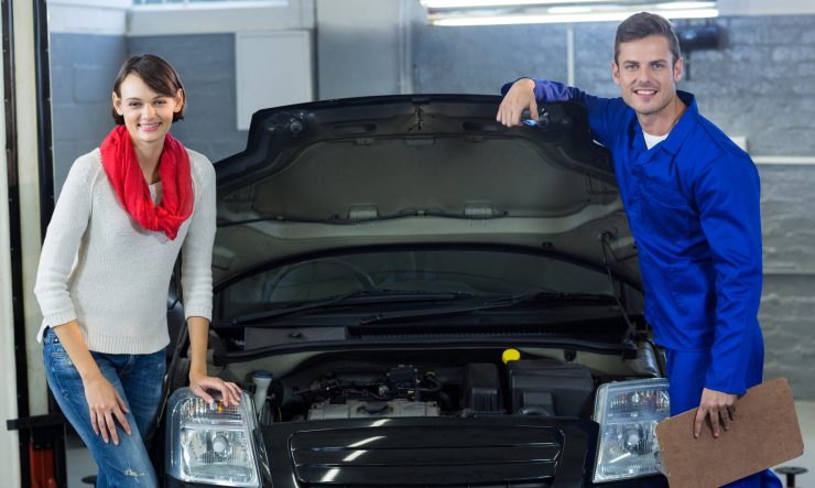 Mechanic and customer standing with car in repair garage
